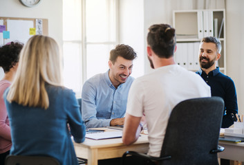 Group of young businesspeople sitting around table in a modern office, having meeting.