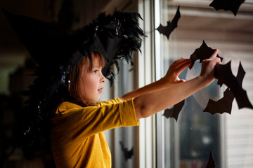 Side view of girl wearing hat sticking bat decorations on window