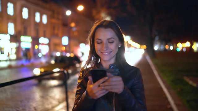 Attractive woman uses a smartphone while walking through the streets of the evening city