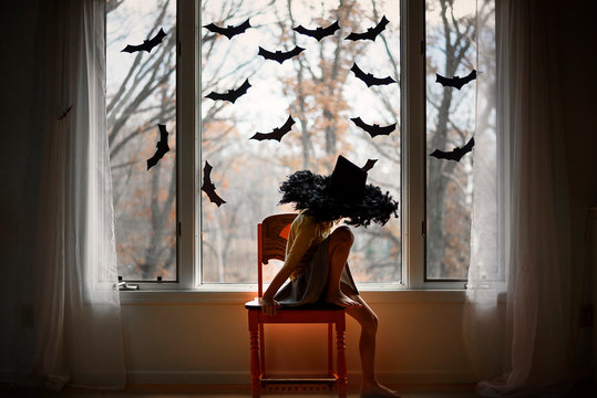 Girl wearing hat sitting on chair by window