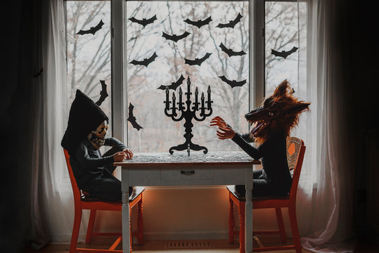 Two children in Halloween costumes sitting by a window doing a puzzle, United States