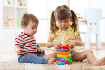 Two children together. The big sister helps the younger brother to assemble the toy pyramid