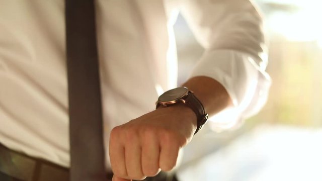 MYKOLAIV, UKRAINE - OCTOBER 12, 2018: Young businessman using Iphone and checking time on wristwatch indoors, closeup
