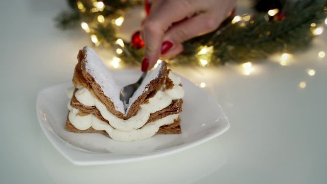 Close up of female hand cutting classic milfey cake with cream in the bowl
