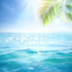 Fototapeta na wymiar Abstract blur defocused background, toned blue, nature of tropical summer with rays of sun light. Beautiful sun glare on sea water and palm leaves against sky. Copy space, summer vacation concept.
