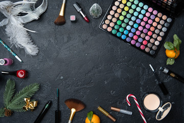 Photo of Christmas tree, mandarin, brushes, lipstick, palette with shadows on black table