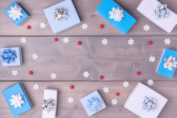 Christmas composition with copy space. Small blue and white boxes with bows, red berries and snowflakes, arranged in a circle on a wooden background. Festive layout.