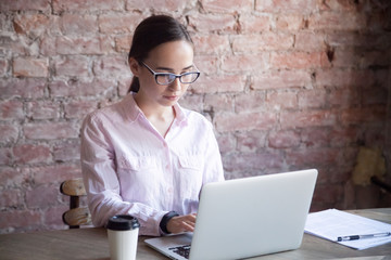 Concentrated businesswoman with glasses looking at laptop. Employee, student performs the task....