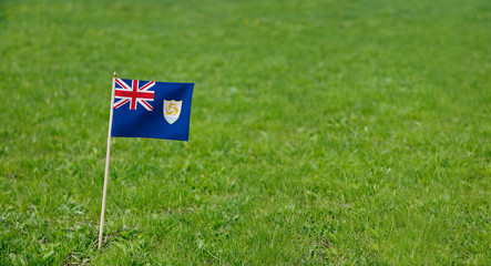 Anguilla flag. Photo of Anguilla flag on a green grass lawn background. Close up of national flag waving outdoors.