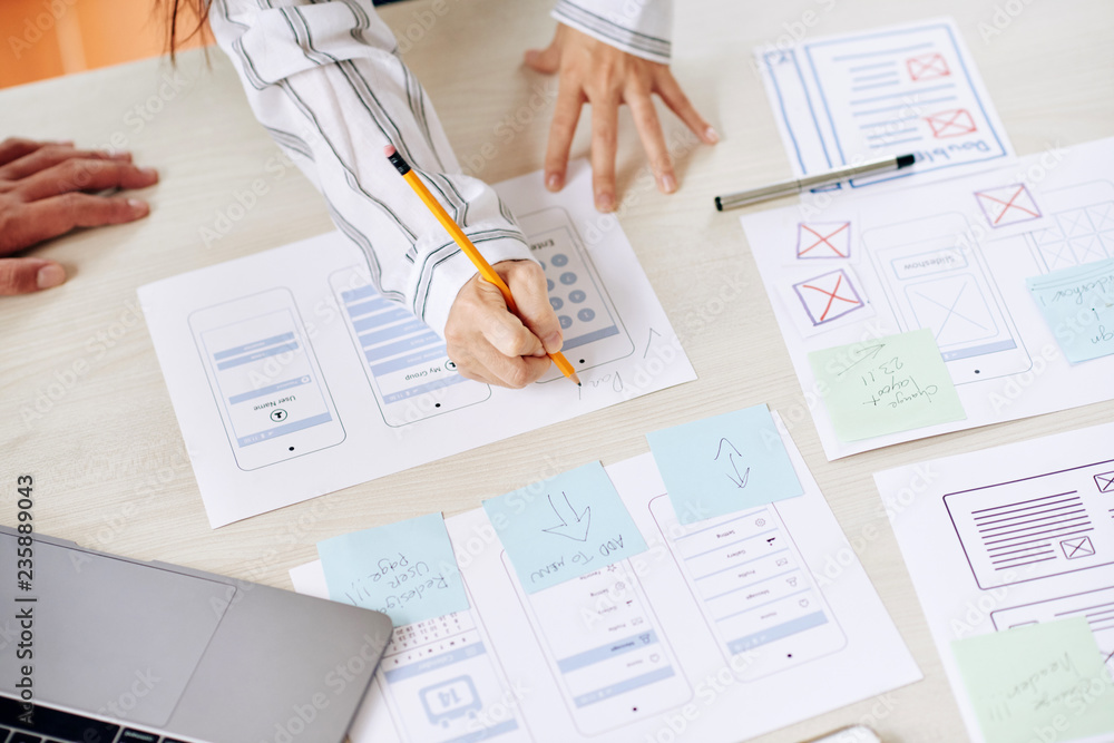 Wall mural crop shot from above of woman drawing on paper making new interface of app with coworker in team