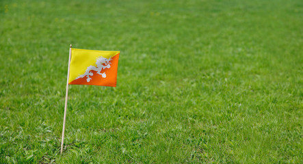Bhutan flag. Photo of Bhutanese flag on a green grass lawn background. Close up of national flag waving outdoors.