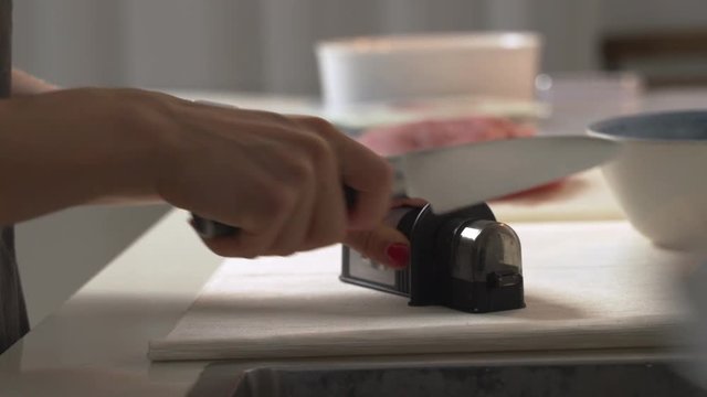 Manual sharpening of a knife in a special sharpener in a kitchen