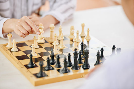 Faceless people playing chess and moving figures on wooden board at table
