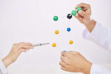 Crop hands of scientists making presentation with colorful molecular model on white backdrop 