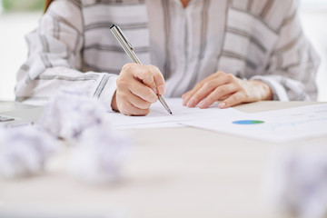 Faceless view of woman in blouse writing on paper document sitting at desk in office