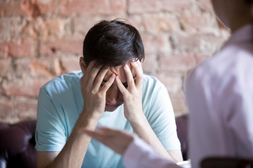 Unhappy young man at a psychologist counselor reception. Upset client covered face with hands....