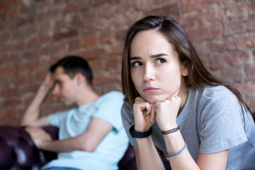 Offended emotional man and woman are seated separately on sofa. Indifferent young couple in...