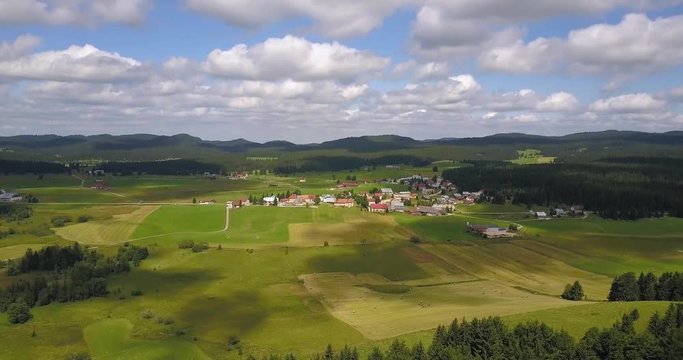 Aerial, drone shot, towards a small town in the french countryside, cloud shadows reflecting on the ground, in Chapelle des bois, Doubs and Jura regional park, Franche comt&radic;&copy;, in France
