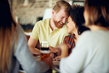 Multi-ethnic couple chatting and drinking wine at reataurant. In foreground their friends. Selective focus on couple.