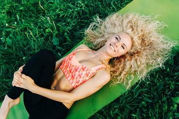 Image of young curly woman lying on sport rug in park
