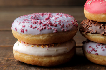 Different sweet donuts with icing and sprinkling close-up stacked on a brown wooden table.