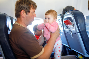 Young tired father and his crying baby daughter during flight on airplane going on vacations. Dad holding baby girl on arm. Air travel with baby, child and family concept