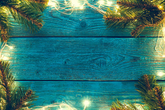 Photo of blue wooden surface with burning New Year's garland around perimeter, with branches of spruce