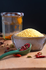 Food concept raw Couscous in brown ceramic bolw and spices on wooden board background