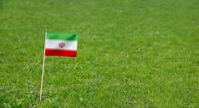 Iran flag. Photo of Iranian flag on a green grass lawn background. Close up of national flag waving outdoors.