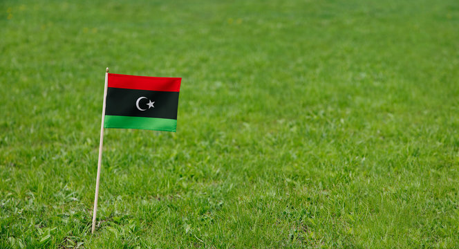 Libya flag. Photo of Libya flag on a green grass lawn background. Close up of national flag waving outdoors.