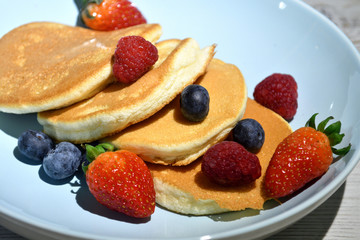 Japanese fluffy pancakes with berries on top on white wooden table.