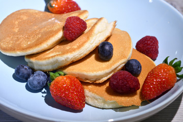 Japanese fluffy pancakes with berries on top on white wooden table.