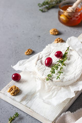 Obraz na płótnie Canvas Baked camembert with cranberry, walnuts, honey and thyme on parchment paper. Brie type of cheese. Grey slate, stone or concrete table. Copy space.