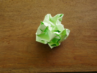 green wrinkled paper ball on wood background, symbol of recycling and wasting our...