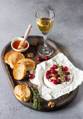 Baked camembert with cranberry, walnuts, honey and thyme on parchment paper. Brie type of cheese. Grey slate, stone or concrete table. Copy space.