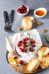 Baked camembert with cranberry, walnuts, honey and thyme on parchment paper. Brie type of cheese. Grey slate, stone or concrete table. Copy space.
