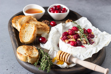 Baked camembert with cranberry, walnuts, honey and thyme on parchment paper. Brie type of cheese. Grey slate, stone or concrete table. Copy space.