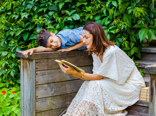 woman and a boy are reading a book on an ancient wooden porch