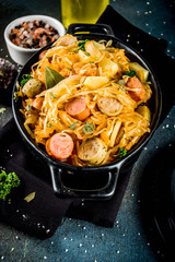 German, polish, Austrian cuisine dish, Bigos - sauerkraut cabbage stewed with meat, mushrooms and sausages, in small pan on dark concrete background.Top view with copy space.