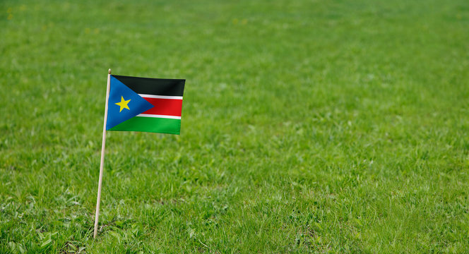 South Sudan flag. Photo of South Sudan flag on a green grass lawn background. Close up of national flag waving outdoors.