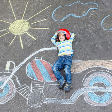 Creative leisure for children: Funny little child of four years in helmet having fun with motorcycle picture drawing with colorful chalks. Children, lifestyle, fun concept