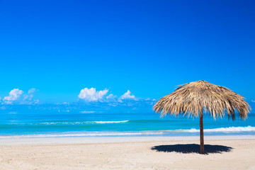 Fototapeta na wymiar Straw umbrella on empty seaside beach in Varadero, Cuba. Relaxation, vacation idyllic background.