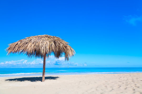 Straw umbrella on empty seaside beach in Varadero, Cuba. Relaxation, vacation idyllic background.