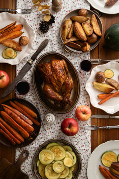 Traditional festive dinner with roasted chicken, apples and verious garnishing on wooden table, covered with patterned tablecloth