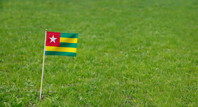 Togo flag. Photo of Togo flag on a green grass lawn background. Close up of national flag waving outdoors.