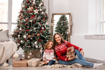 Obraz na płótnie Canvas Happy mother and daughter seating near fir-tree.