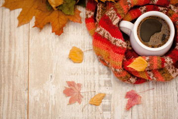 Naklejka na ściany i meble A cup of coffee wrapped in a scarf on a table covered with colorful leaves.