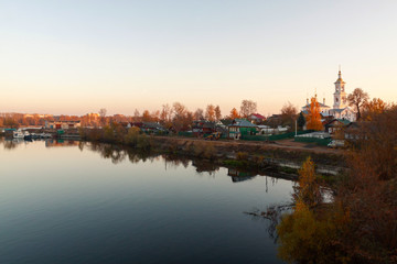panoramic view of the church which is situated on the bank of the river among private houses against the background of blue sky reflected in water
