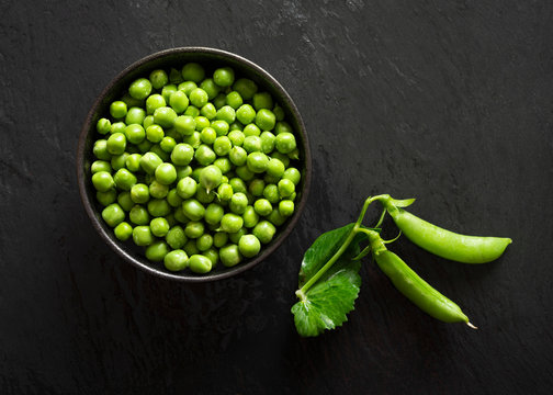 A bowl of fresh green peas with two pea pods.