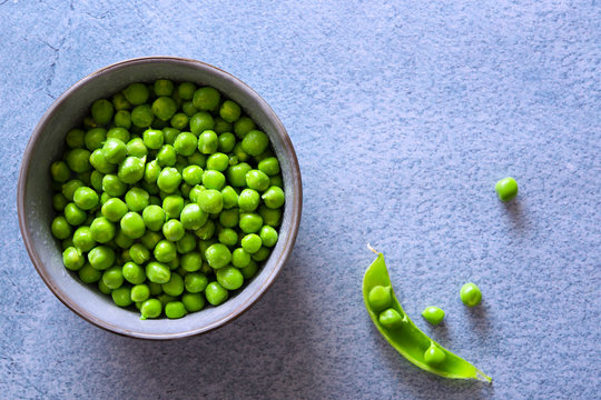 Raw green peas in a bowl and an open pea pod.